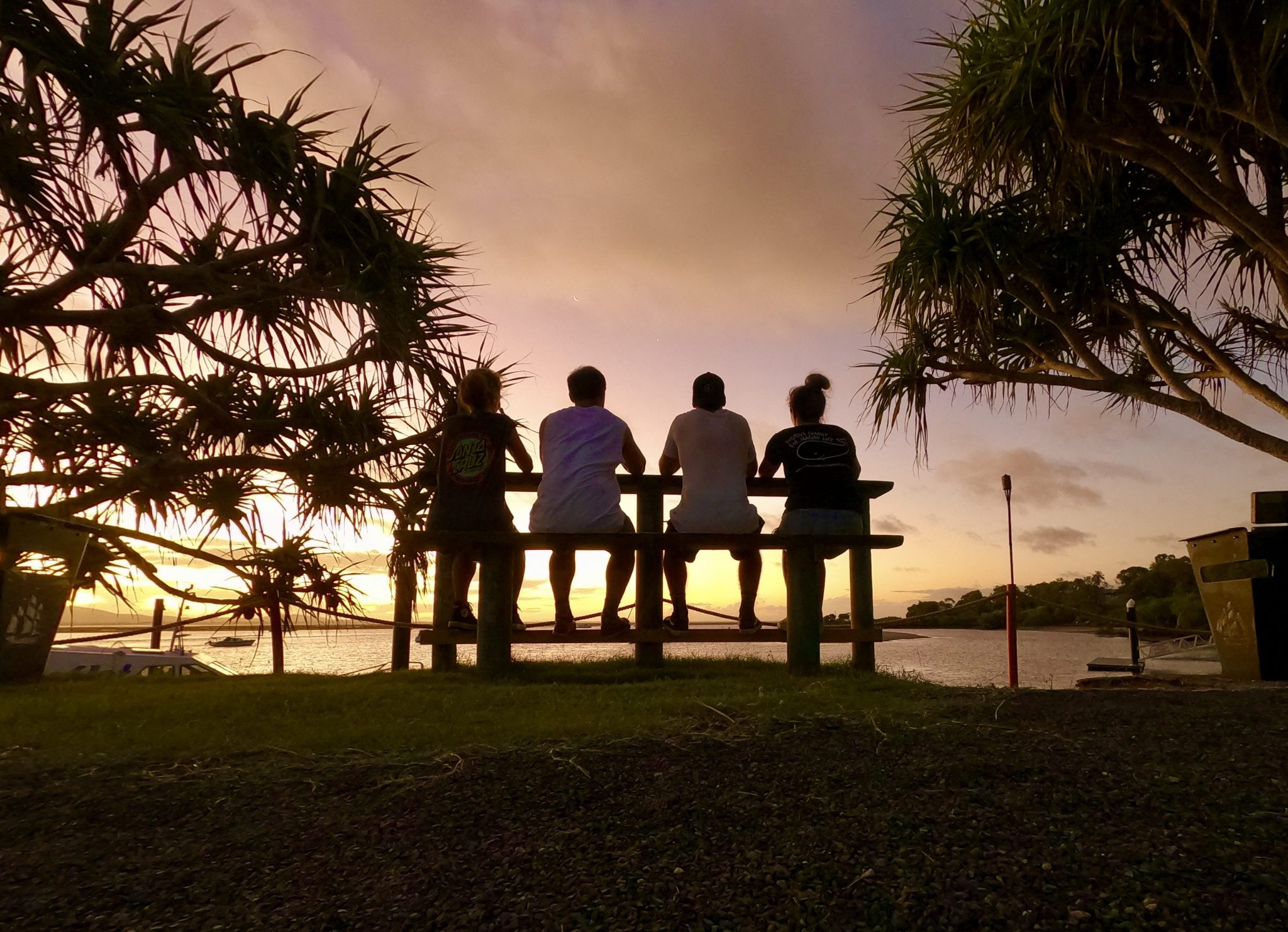 Four friends watching the sunset over the water at a tall bench at the 1770 Marina.