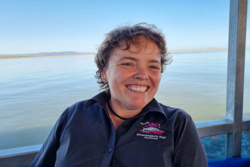 Staff member smiling at camera with ocean in the background.