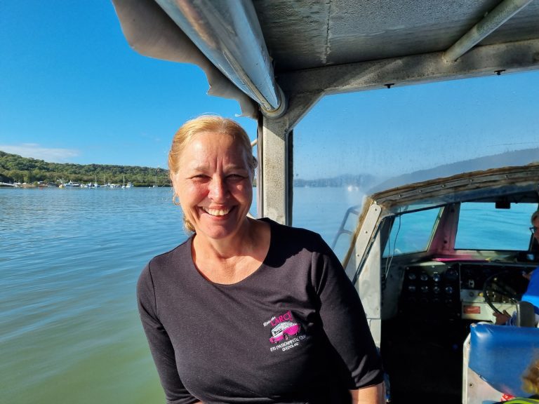 Staff member of LARC Tours, smiling at camera, on the LARC with ocean and blue skies background.