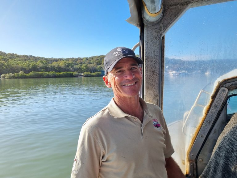 Photo of LARC tours owner smiling at the camera with ocean in the background and blue skies.
