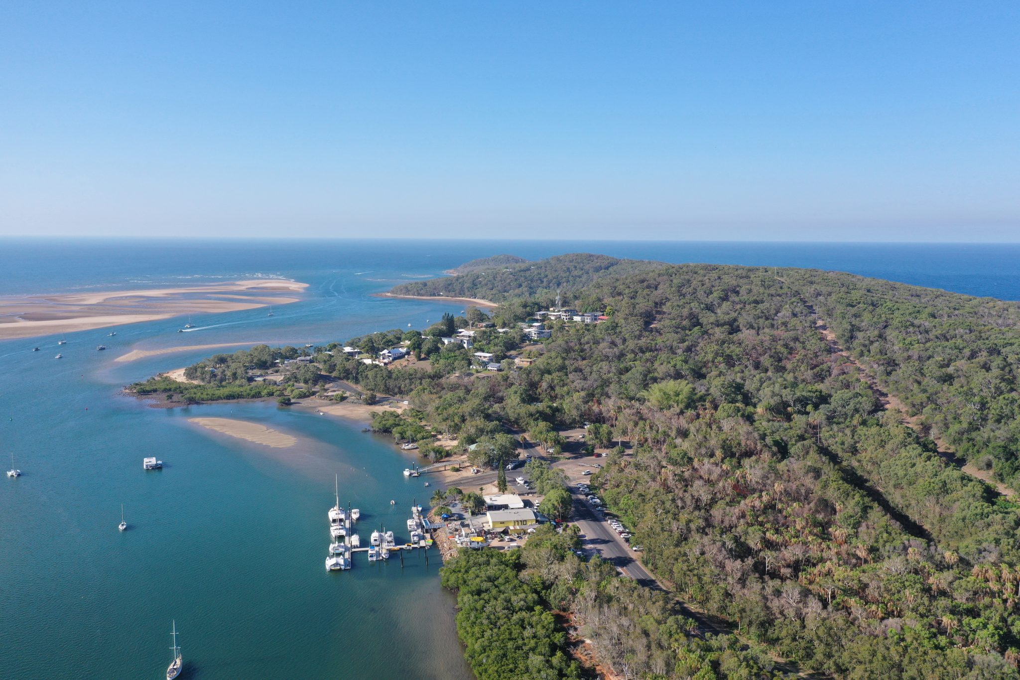 An aerial photo of the 1770 Marina, including boats, houses and shops. Round hill creek, the 1770 headland and the ocean.