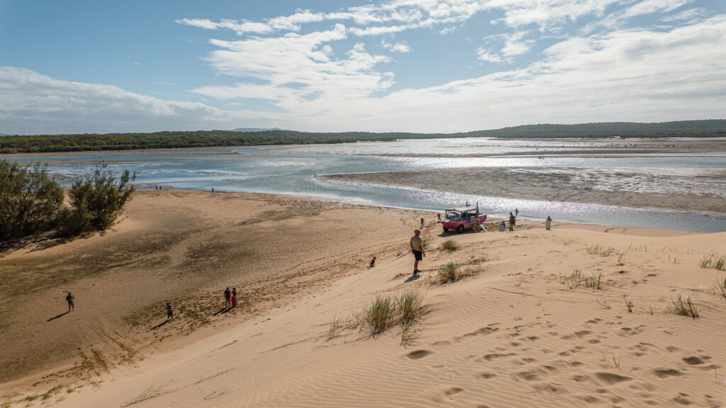 Sloping sand dunes, tidal creek and people preparing to sandboard